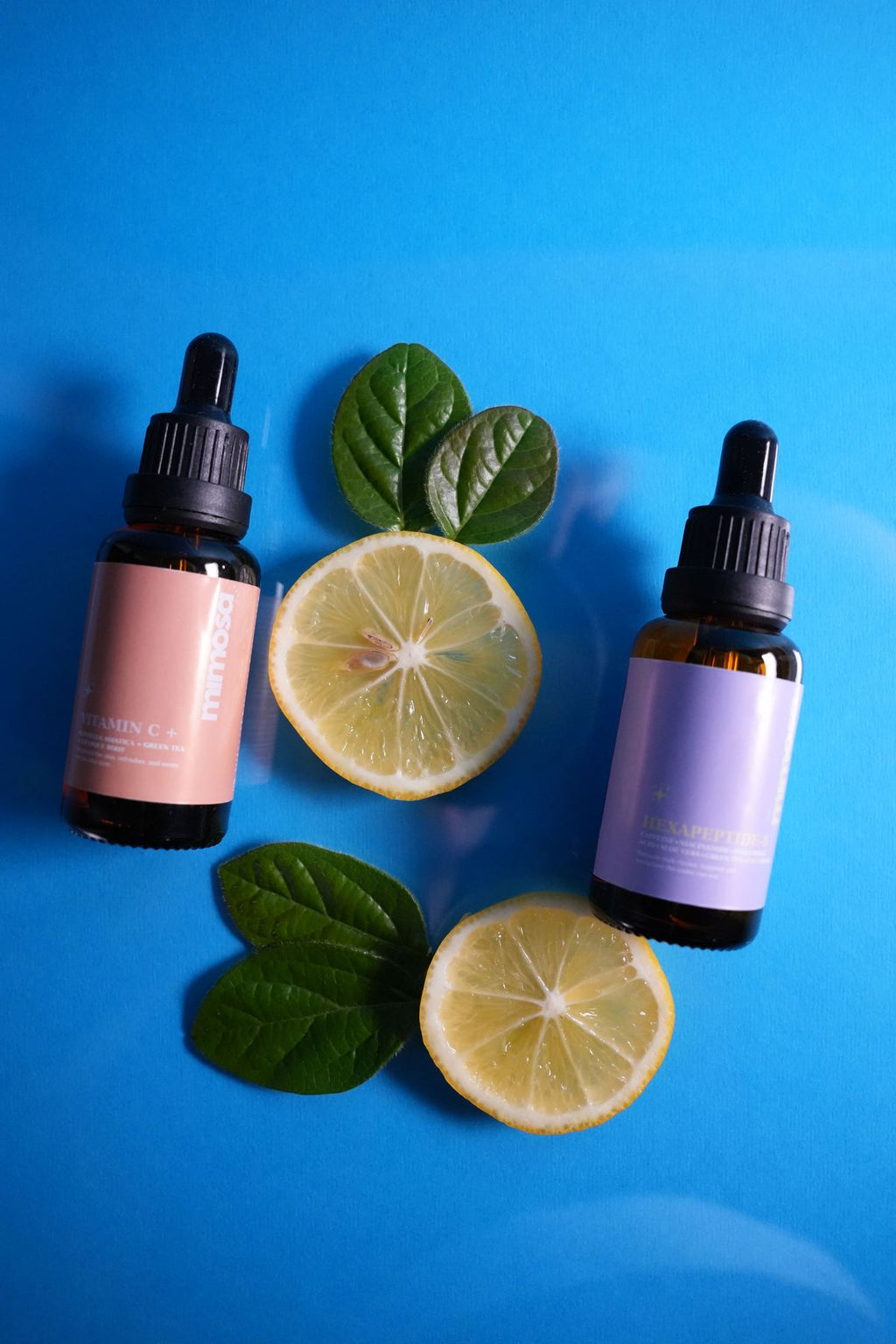 Two amber dropper bottles with lemon slices and green leaves on a blue background