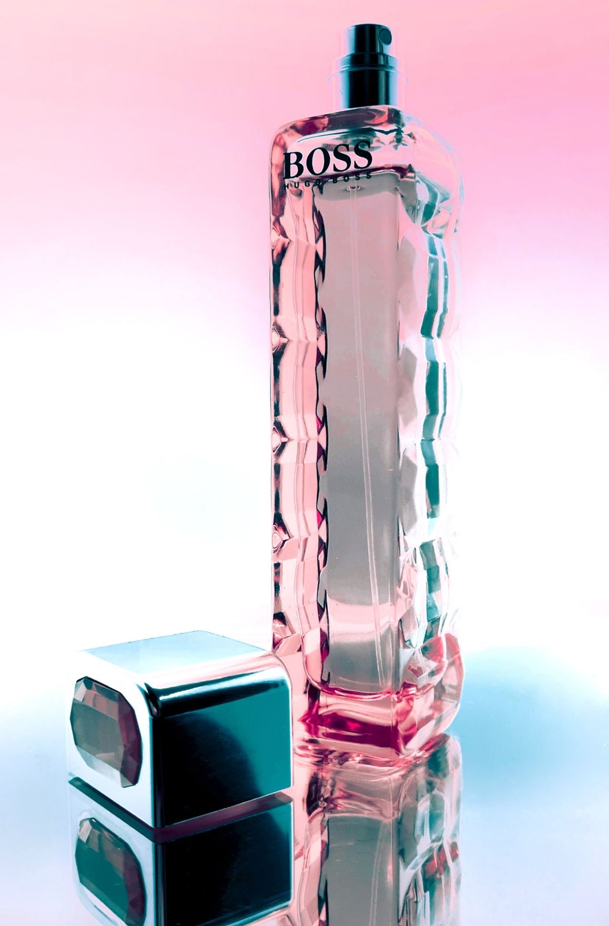 Hugo Boss perfume bottle with cap beside it on a pink and blue reflective surface