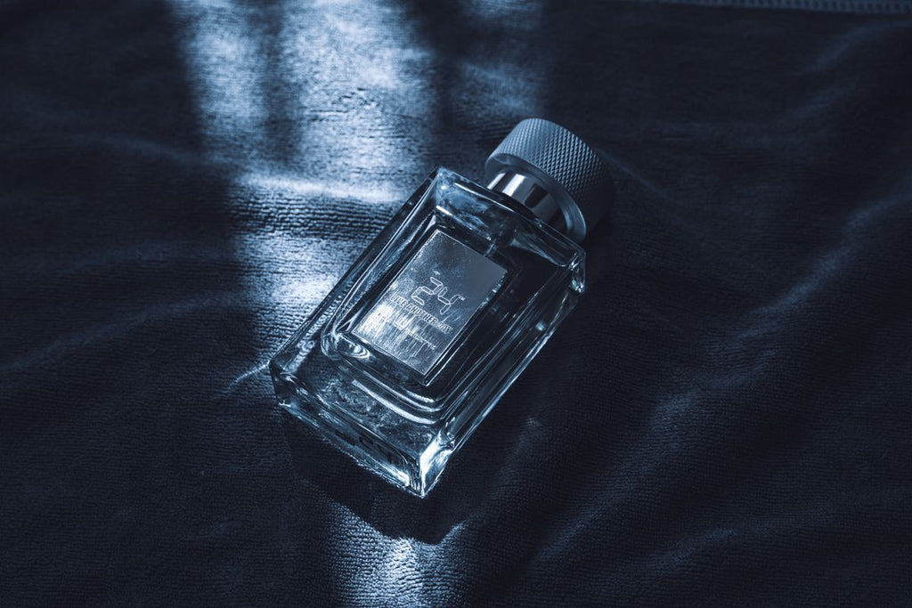 Clear rectangular perfume bottle with a silver cap lying on dark fabric