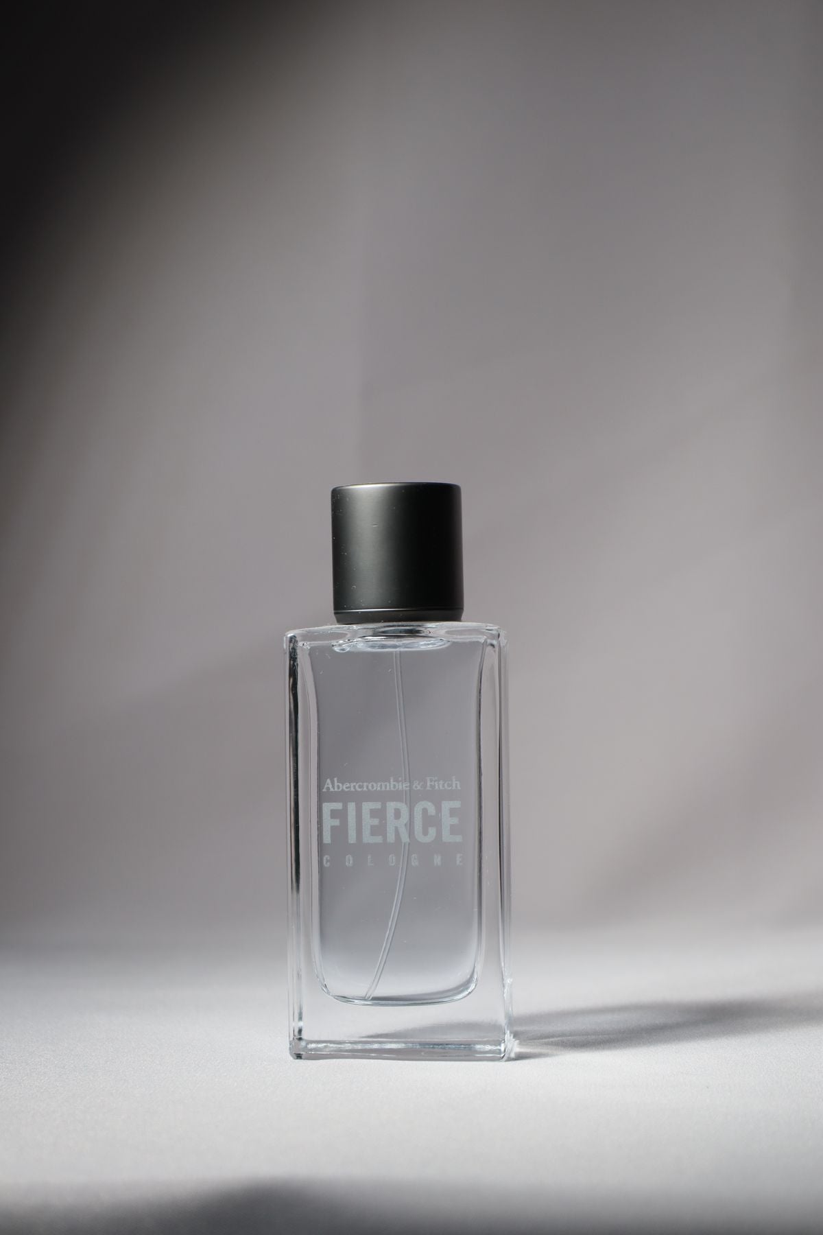 Clear rectangular fragrance bottle with black cap on a gray studio backdrop