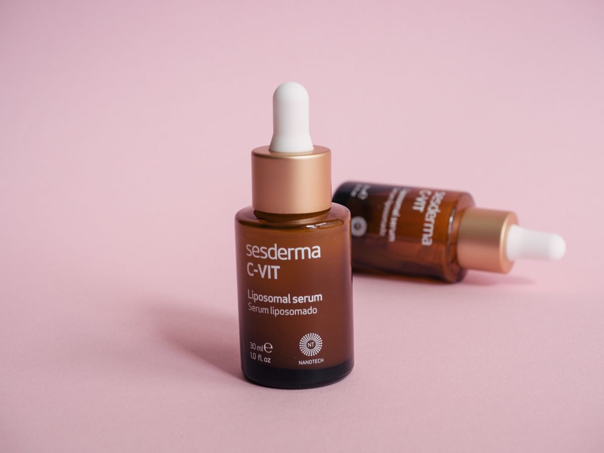 Two C-VIT serum dropper bottles on a pink surface, one upright and one lying down