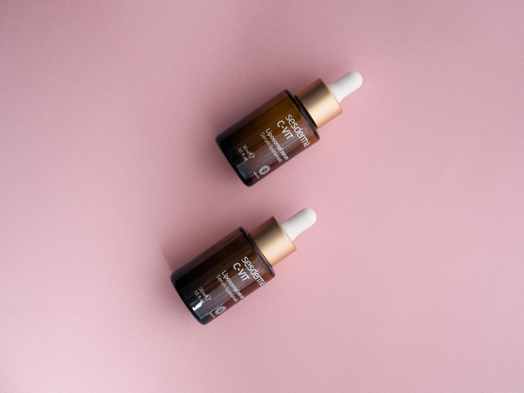 Two amber C-VIT serum dropper bottles laid diagonally on a pink background