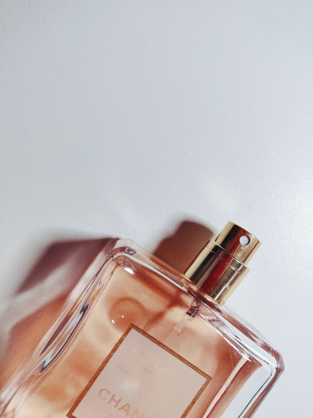 Cropped peach-toned perfume bottle with gold spray nozzle on a white surface