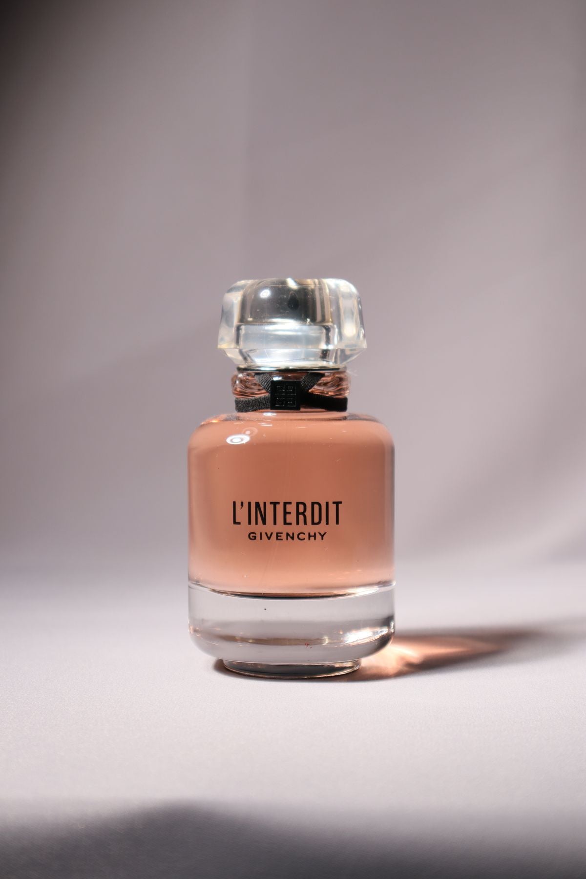 Pink Givenchy L'Interdit perfume bottle with a clear cap and black bow detail