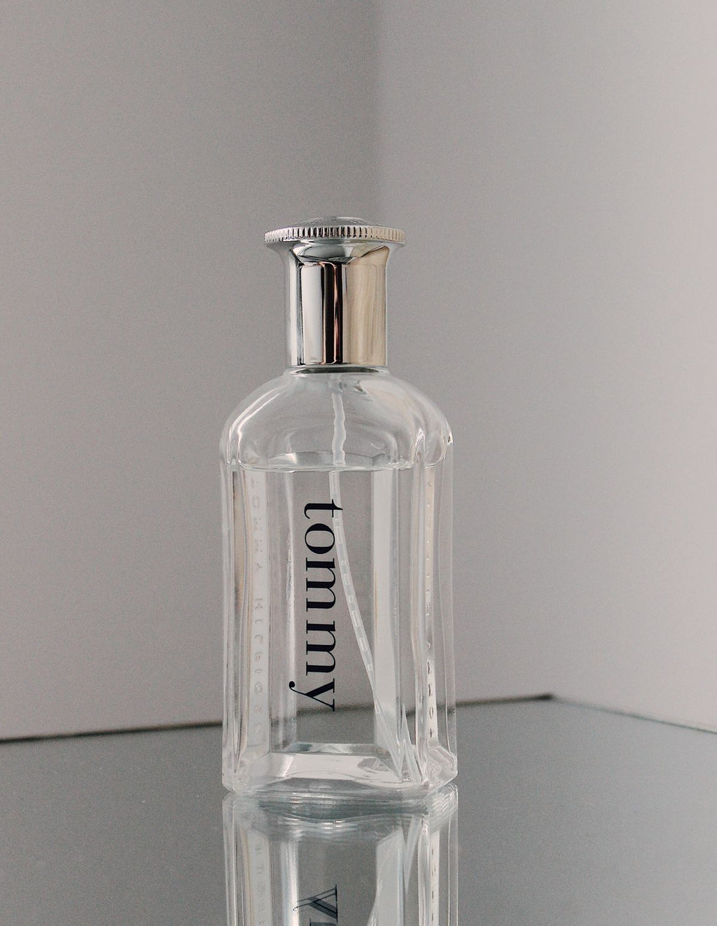 Clear fragrance bottle with ribbed glass sides and silver cap on a reflective surface
