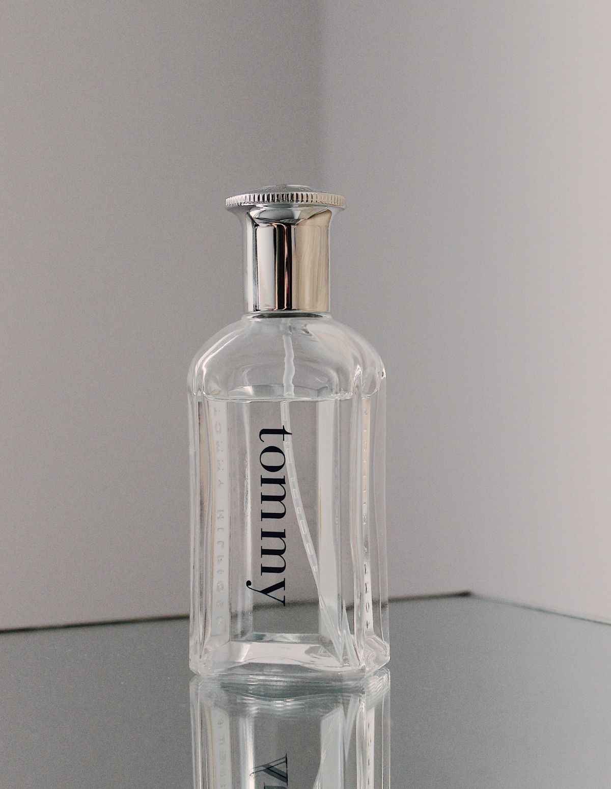 Clear fragrance bottle with ribbed glass sides and silver cap on a reflective surface