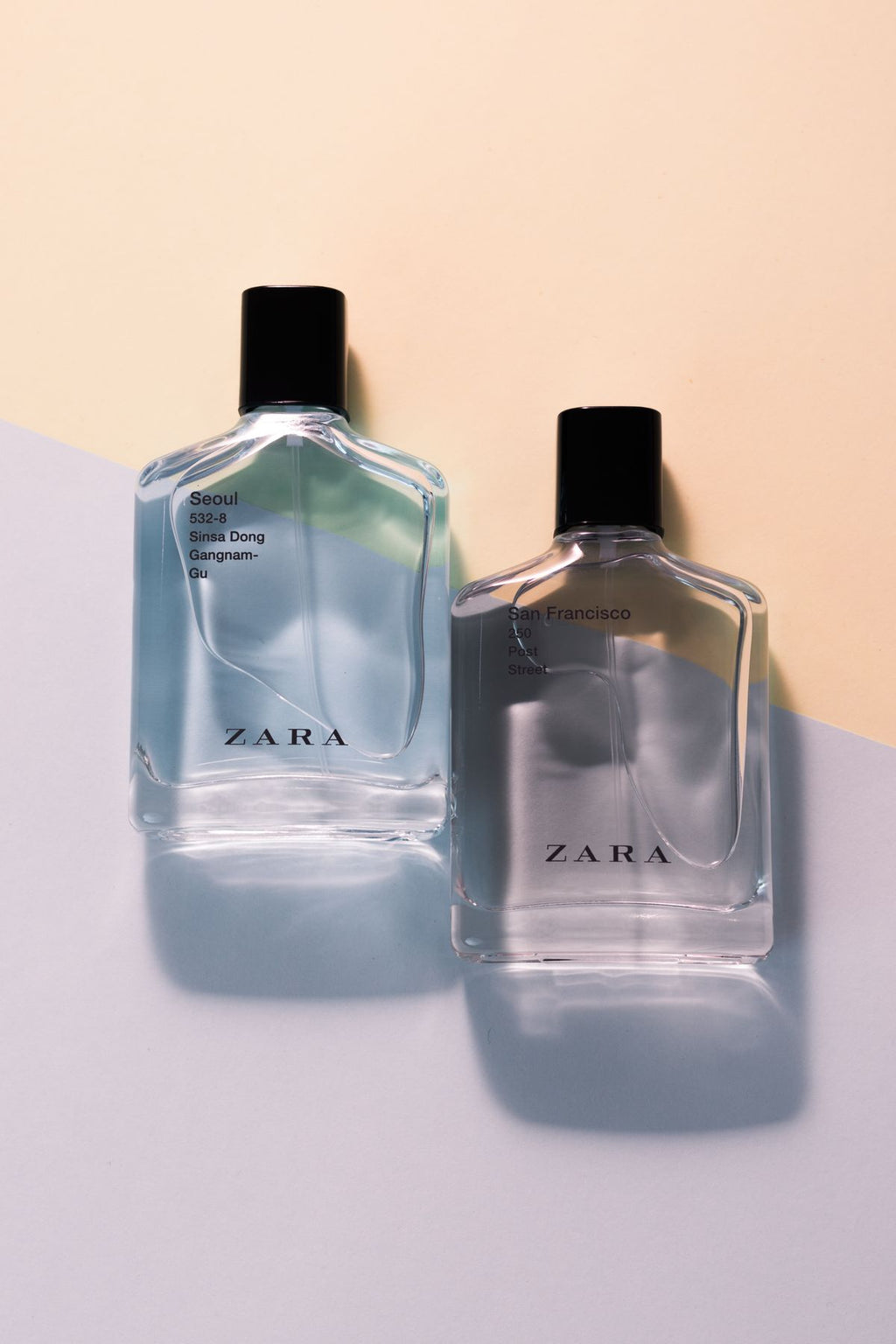 Two clear perfume bottles with black caps on a pastel split background